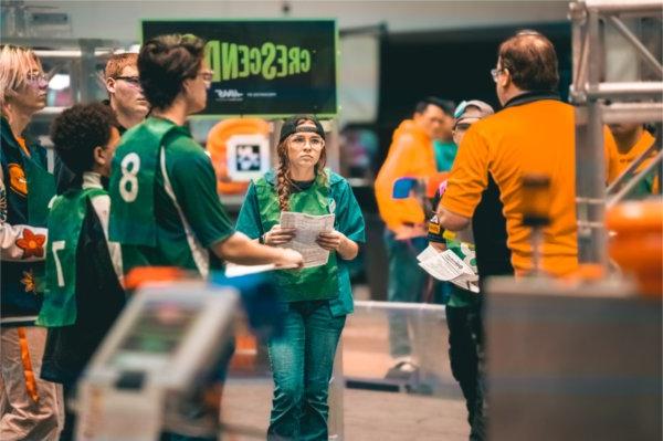 在机器人活动中，穿绿色t恤的队员向穿橙色t恤的教练咨询
