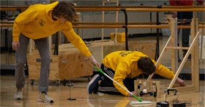 机器人比赛期间，两个穿黄色衣服的学生在地板上工作，其中一个拿着更快的拖把